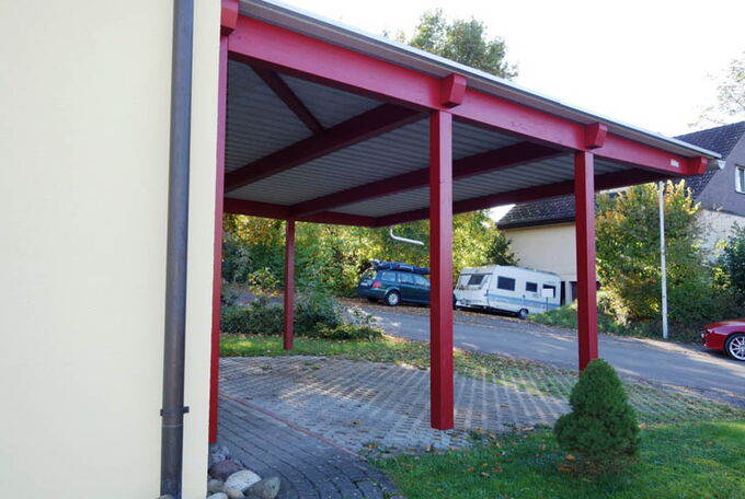 Schützende Parkplatzüberdachnung mit roten Stützen und Trägern, Wellblechdach