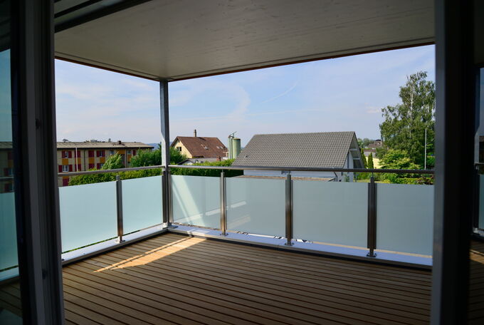 Gedeckter Balkon mit Milchglasgeländer und ruhiger Holzbodenbelag
