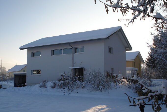 Ansicht der Hausfassade eingangseitig, lange schmale Fenster wurden hier verbaut, Haus mit Winterkleid und von der Sonne beschienen fotografiert