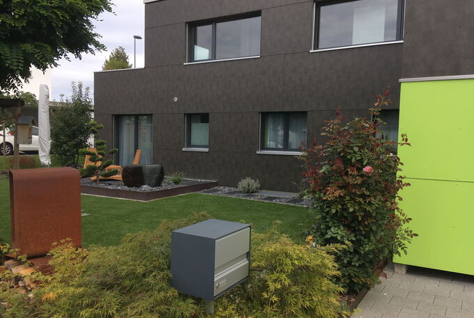 Hausansicht mit Gartenteil, Sitzplatz mit Lounge und schönem Steingarten, geschützt wird der Garten durch eine gemischte Pflanzenhecke