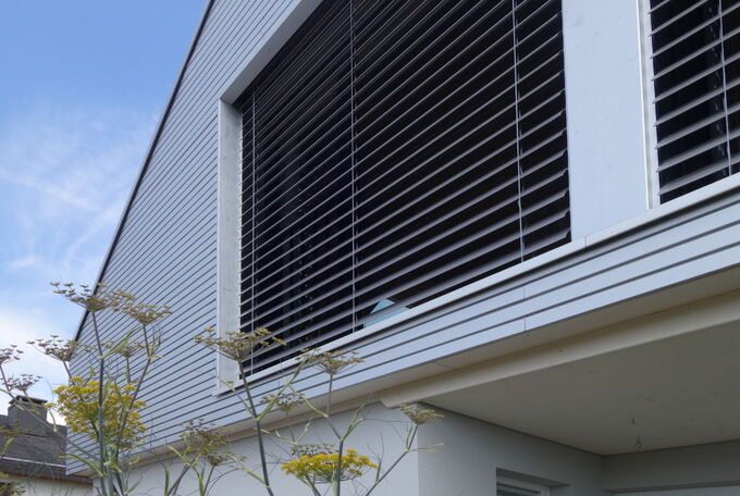 Fassadenansicht einer Aufstockung mit silberner Holzschalung und passender Lamellenstore