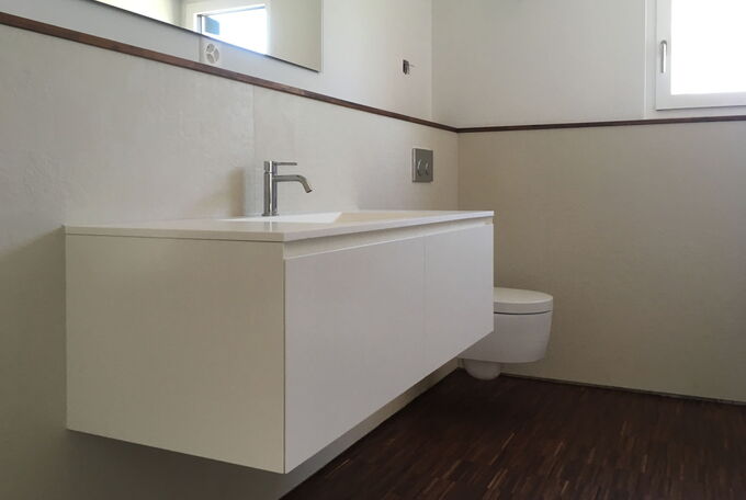 Badezimmermöbel mit integriertem Waschbecken, grossformatige Wandplatten, dunkler Stabparkett