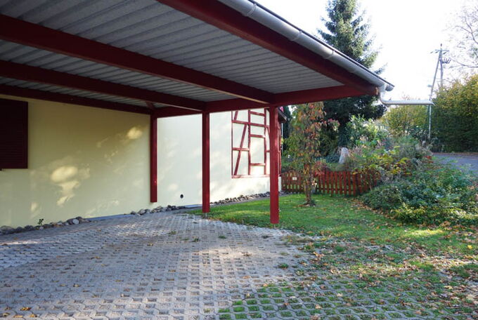 Parkplatzüberdachung mit grossem auskragendem Vordach, Holzkonstruktion in Rot, Trapezblech mit Rinne und Wasserspeier