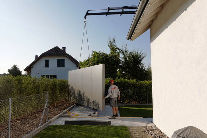 Holzelement der Rückwand für Gartenhaus wird mit dem Kran auf Bauplatz versetzt