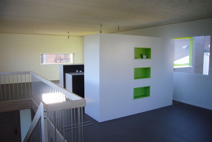 Helle Küche freistehend im Raum als Raumtrenner, grüne Details bei der Küche als Wiederaufnahme der grünen Fassadenelemente