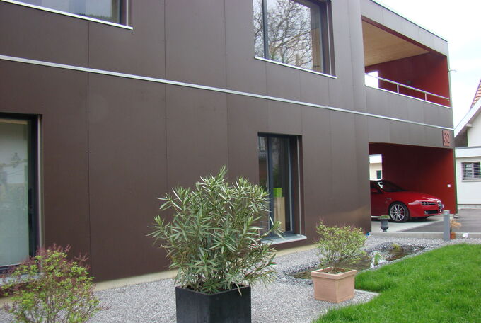 Detailansicht dunkelbraune Fassade mit Abschlussleiste zwischen den Fassadenplatten in Chromstahl